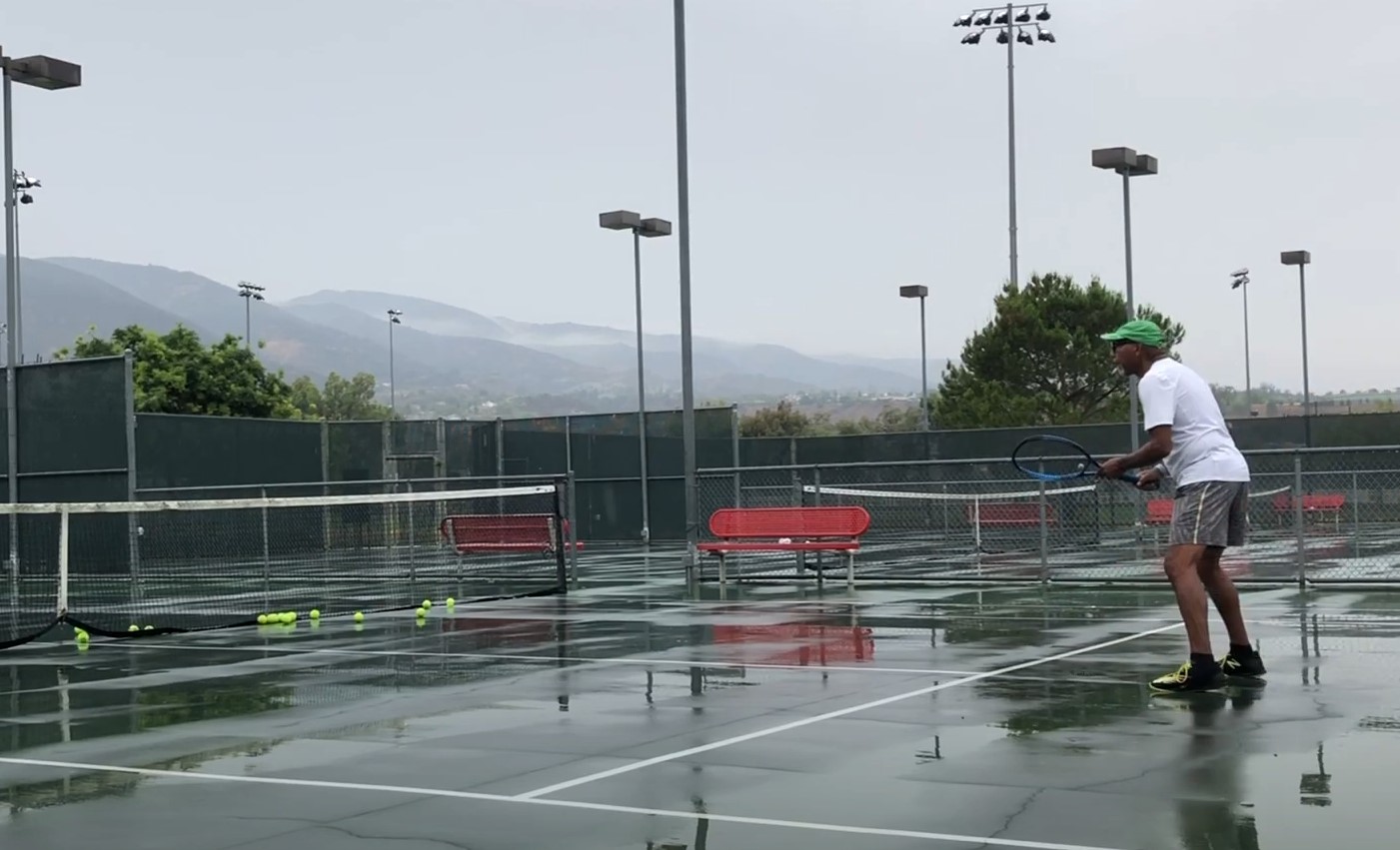 man playing tennis on a court soaked by rain